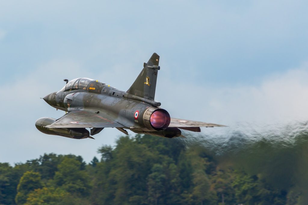 Camouflage single engine fighter jet ascending with afterburner flame 